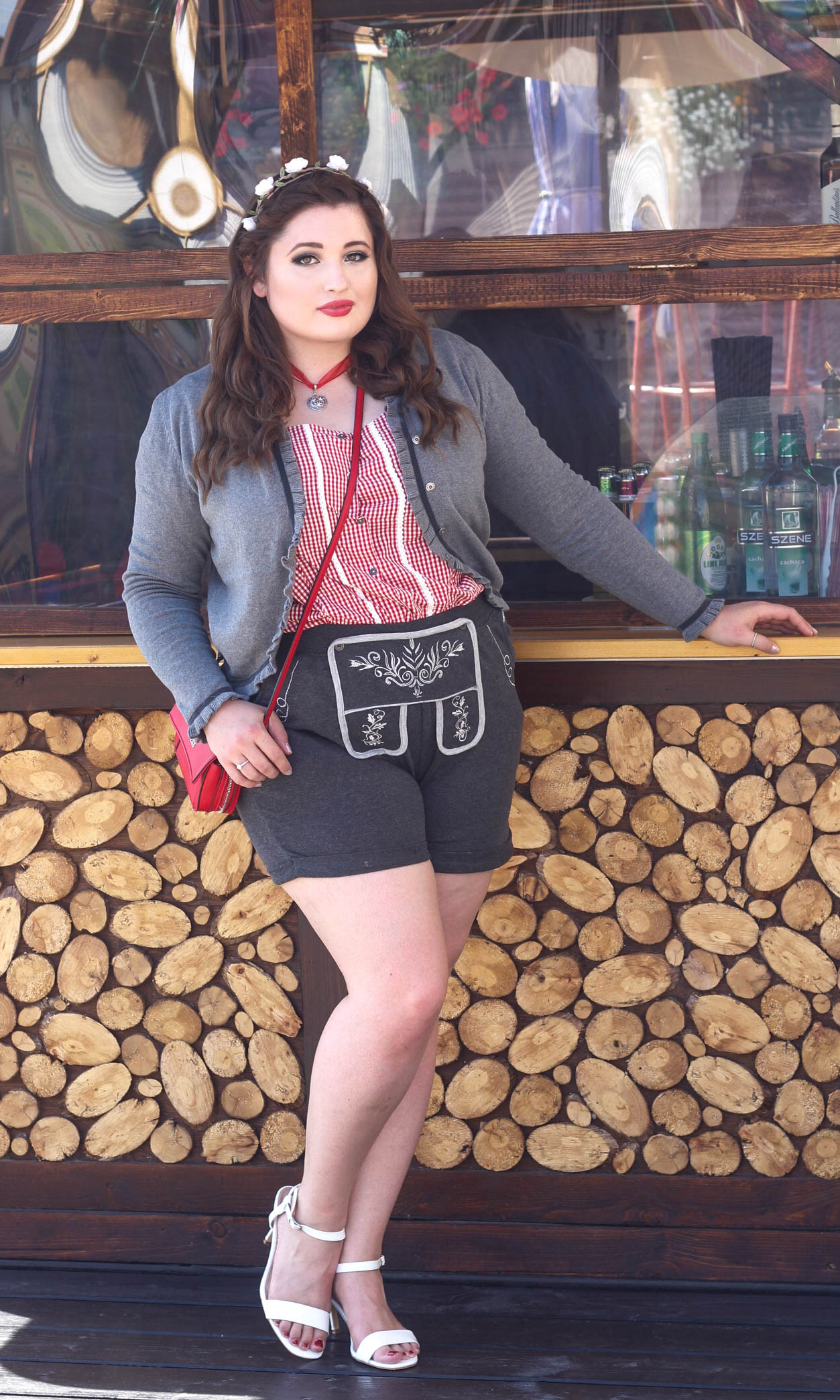 Junge kurvige Frau vor einer Holzhütte im Oktoberfest Outfit. Plus Size Lederhosen Look.